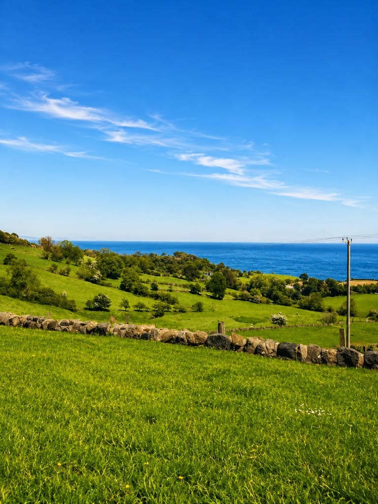 Blue-sky coastal view across green fields in the Glens of Antrim
